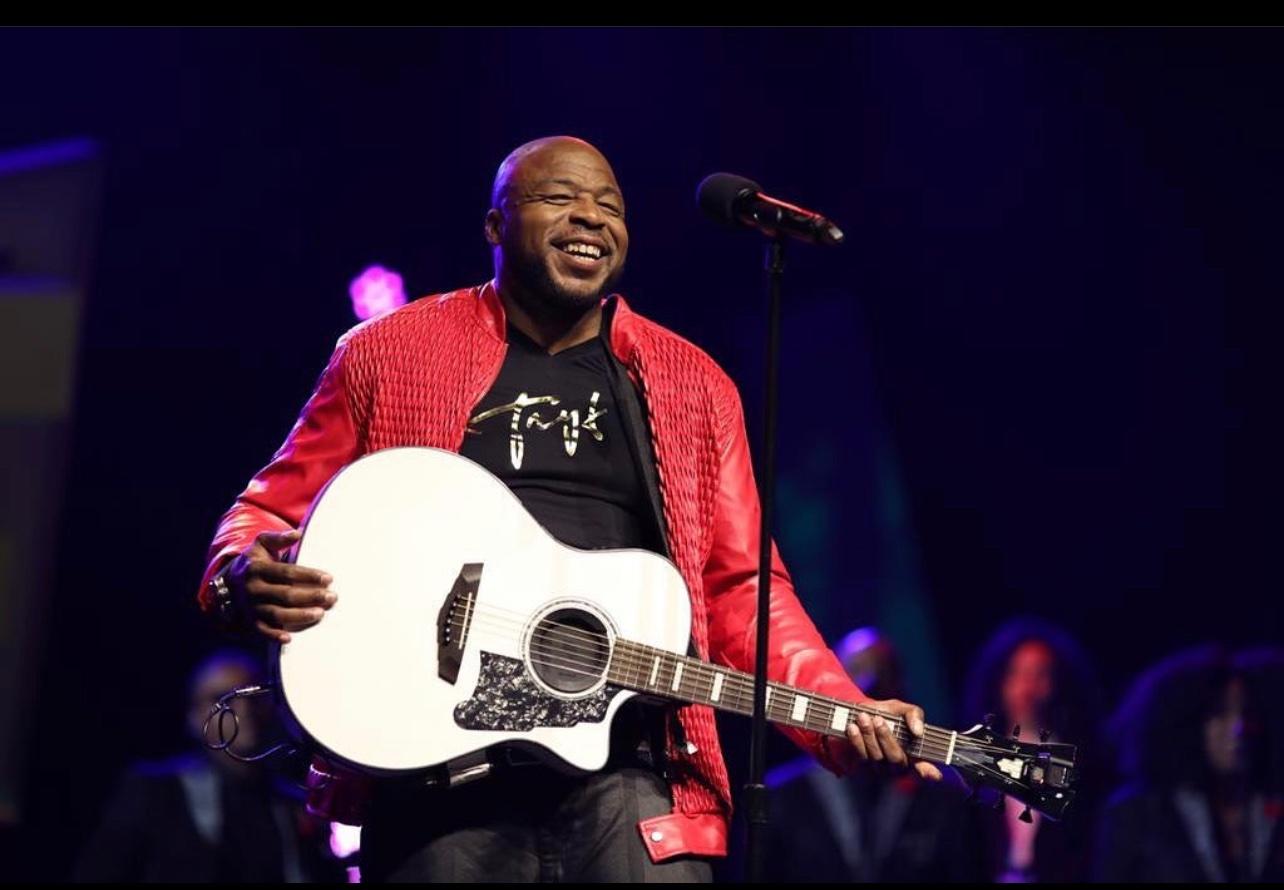 Tryf Da Comedian performing on stage with a white acoustic guitar